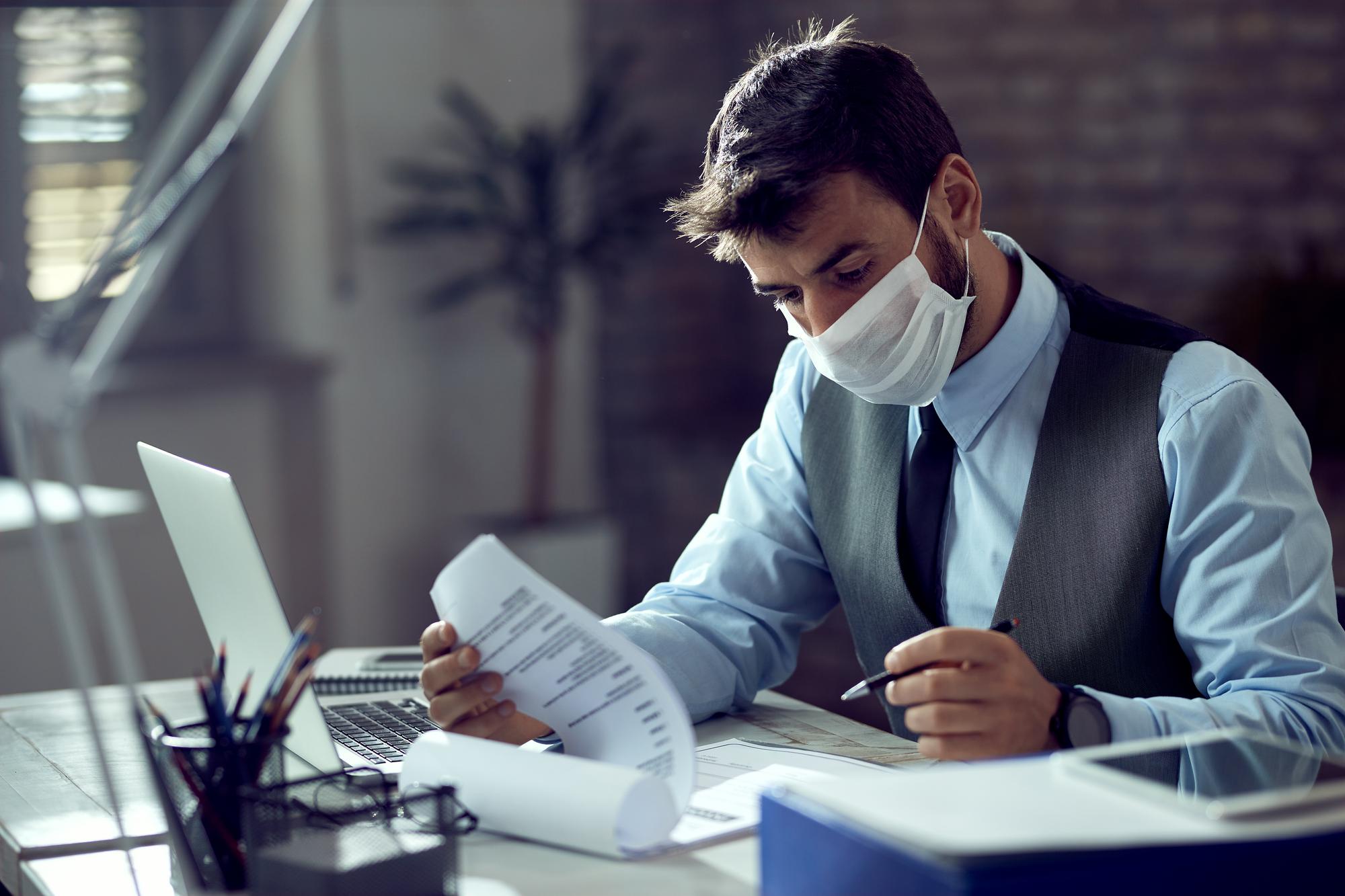 male-entrepreneur-analyzing-business-reports-while-wearing-face-mask-working-office-during-virus-epidemic_637285-6349
